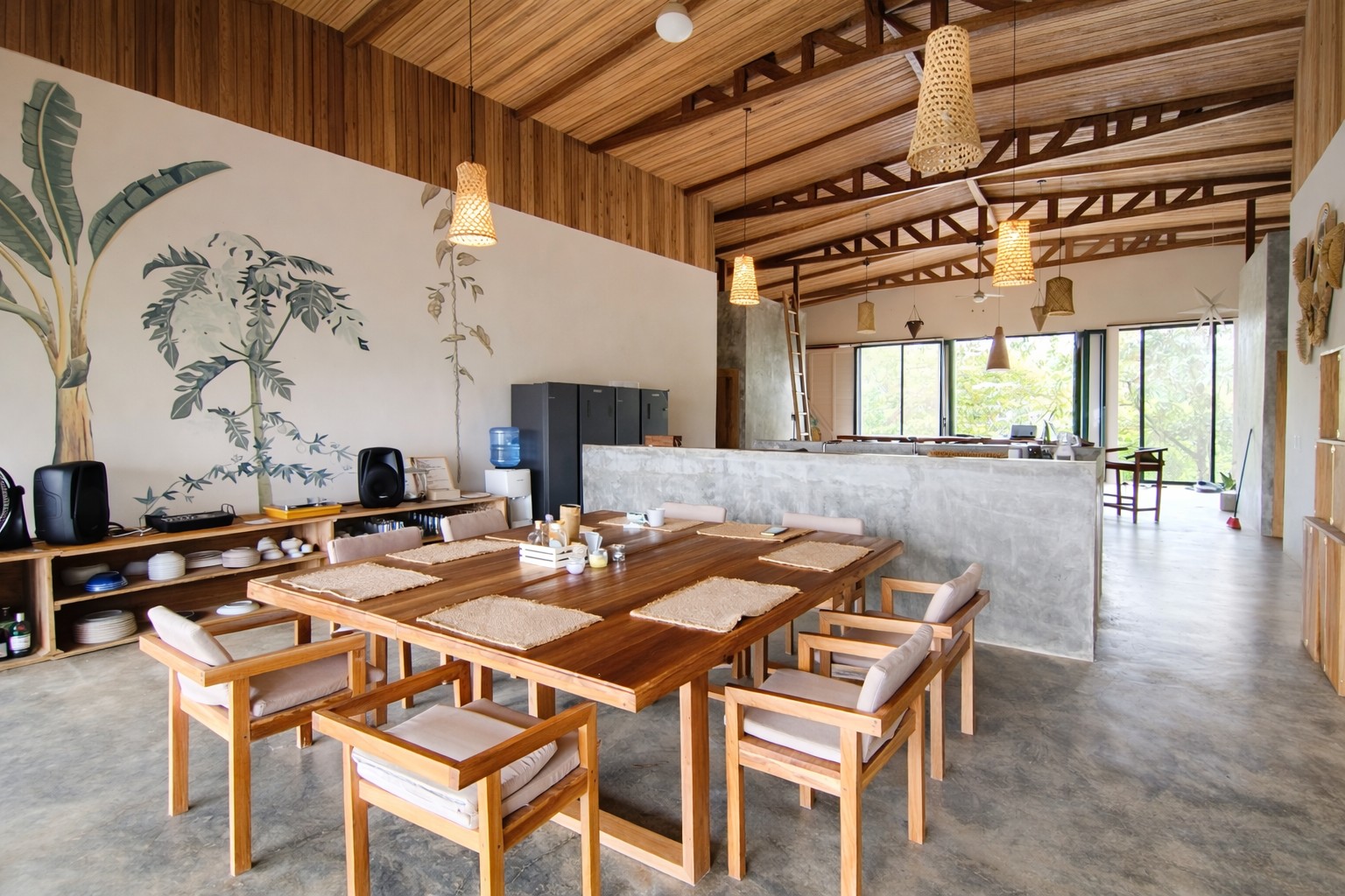Comedor con mesa de madera y mural de plantas, con la cocina abierta al fondo