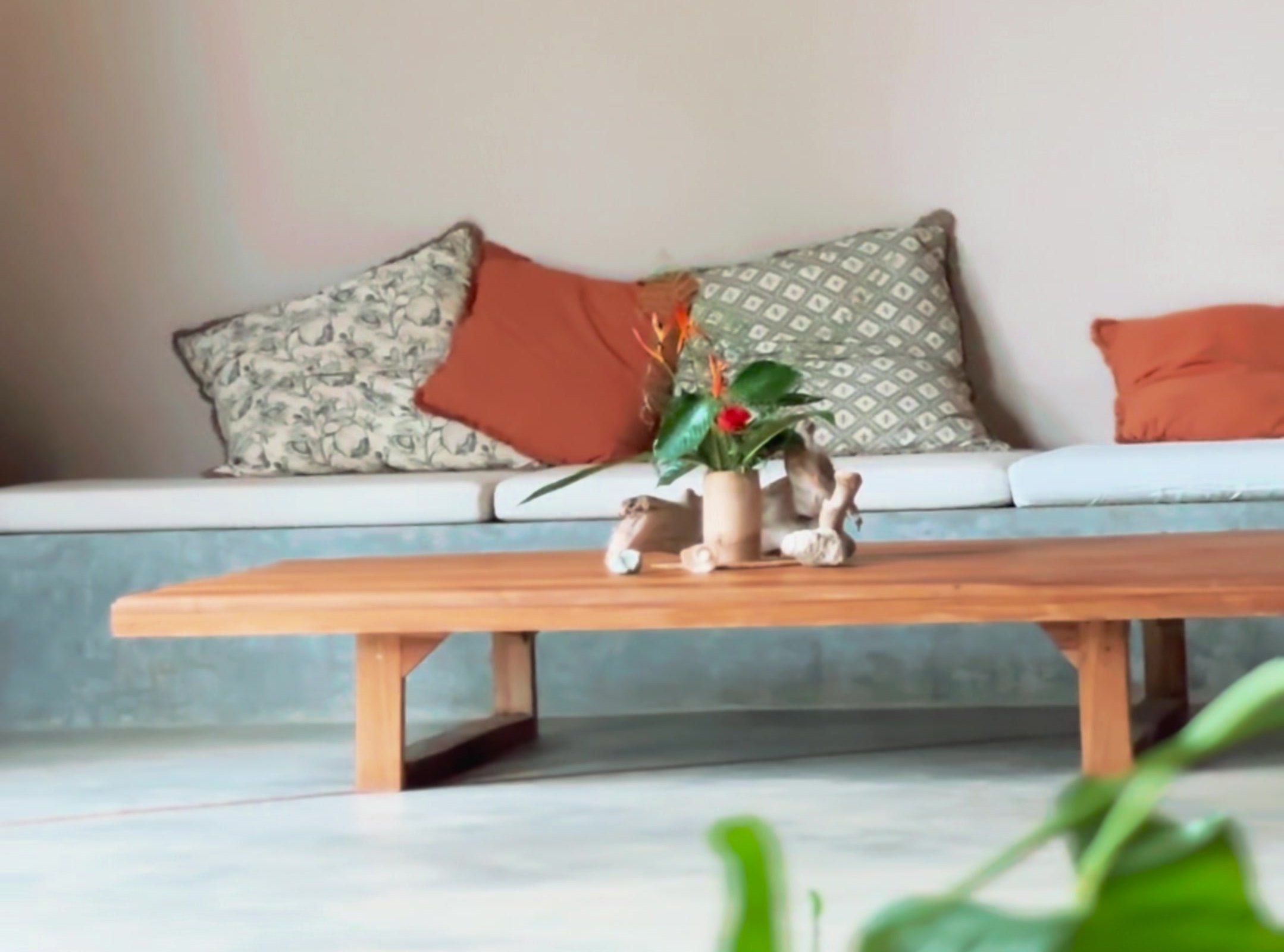 Sofá de obra con cojines de colores, mesa baja de madera y flores
